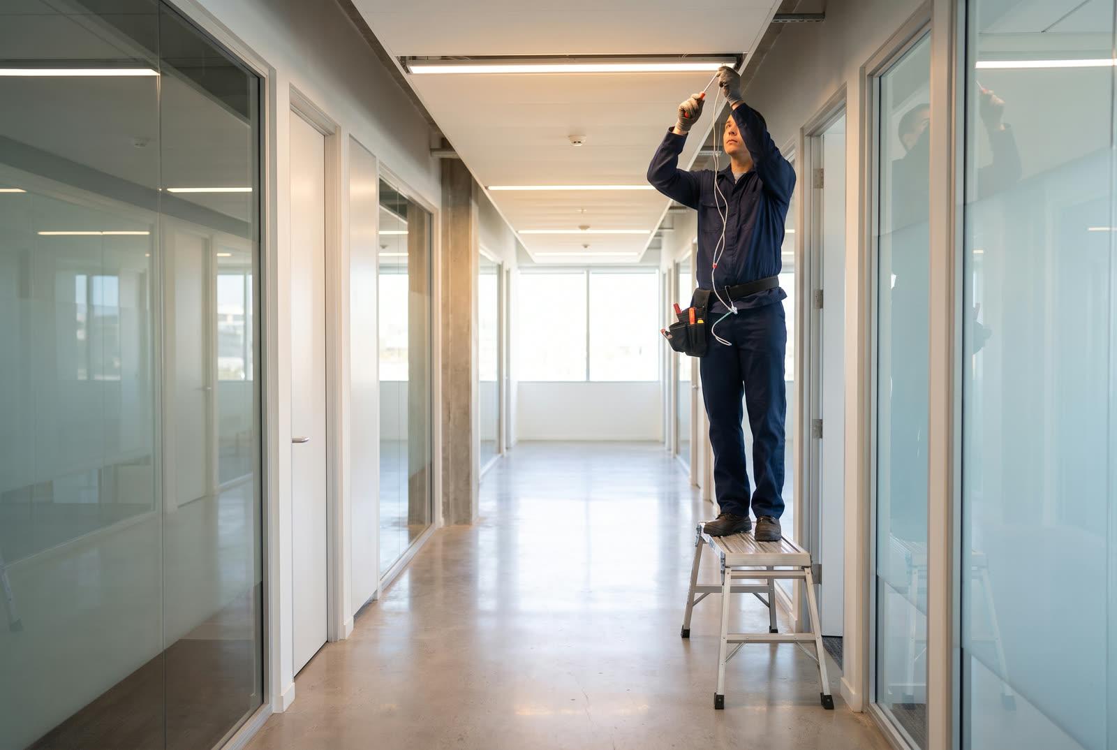 Facilities technician performing maintenance in a modern commercial office corridor under clean professional lighting