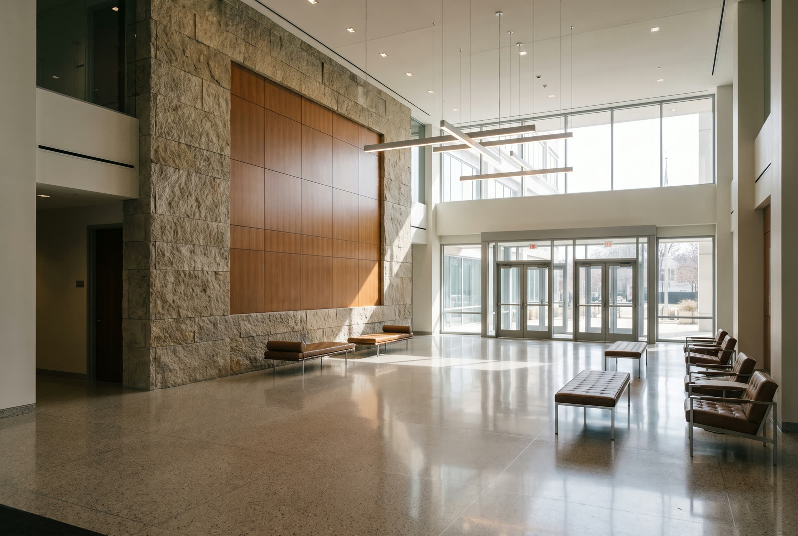Modernized multi-tenant office building lobby with new stone-look flooring, wood-slat feature wall and recessed lighting, with a protective floor covering and a worker in a hard hat and high-visibility vest at the far end